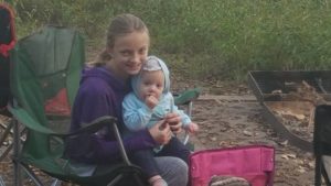 Girl hoding a baby at camp site.
